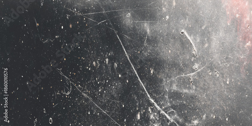 A textured dark gray surface displaying prominent scratches and speckled imperfections with hints of red undertones