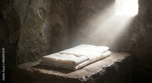 Folded white linen burial cloth lying on stone slab in empty tomb with sunbeam light representing Jesus resurrection