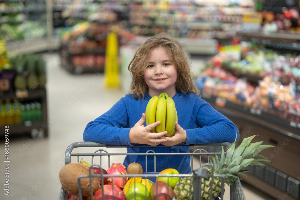 Fototapeta premium Children picking fresh fruits in the supermarket. Healthy vegetables in a kids shopping cart. Kid groceries at the market. Kid in a supermarket. Child shopping vegetables. Grocery shopping with kids.