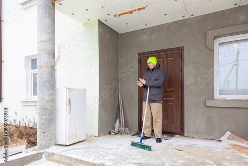 man swept snow off the porch of his country house, shaking off his hands after working in the winter weather.