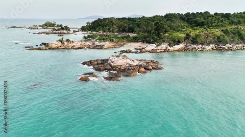 Aerial view of a beautiful tropical coastline with clear turquoise water, rocky islands, and lush green vegetation under a bright sky.