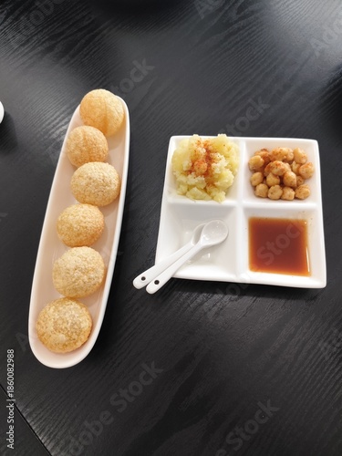 Pani puri is served on a white ceramic plate with side dishes of mashed potatoes, chickpeas, and sweet sauce.