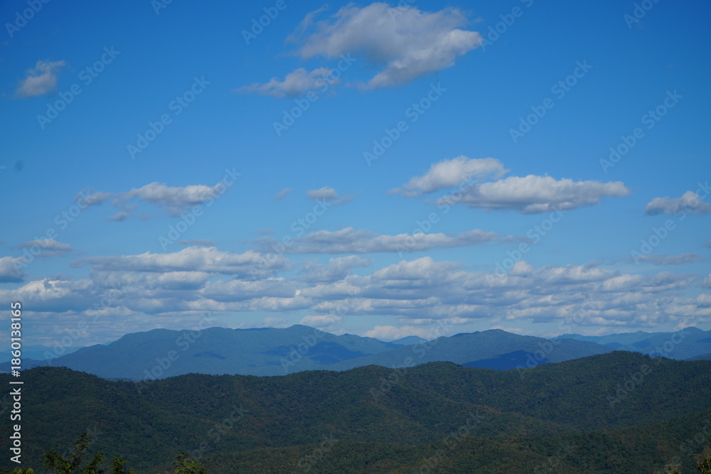 Naklejka premium Mountain Range Under Clear Blue Sky with Soft Clouds