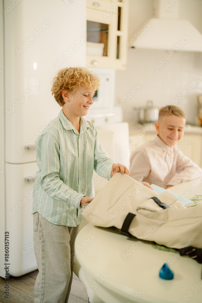 Obraz premium Two children engage in a fun activity in a bright kitchen. One child is organizing a backpack while the other sits and smiles, creating a cheerful atmosphere.