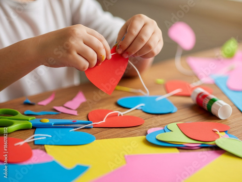 Child hands creating colorful paper hearts at wooden table, craft activity supports creativity, craft process fits education themes, craft visuals ideal for childhood learning and family lifestyle