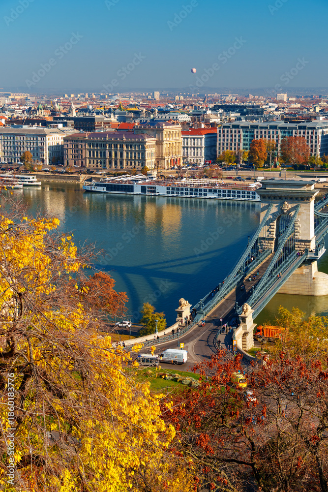Obraz premium Budapest cityscape, panoramic view of city and Danube River with Chain bridge and beautiful architecture in autumn season, trees, branches and yellow leaves in foreground