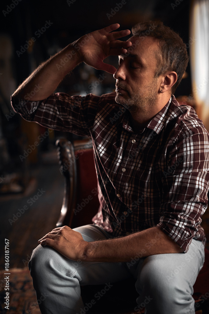 Obraz premium Man with headache, depression, sadness and loneliness sitting on a chair at home.