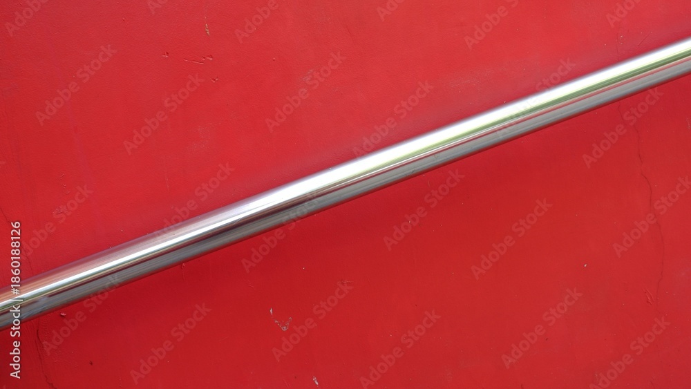 Αυτοκόλλητο Abstract minimalist close-up of a polished chrome handrail diagonally crossing a vibrant solid red wall