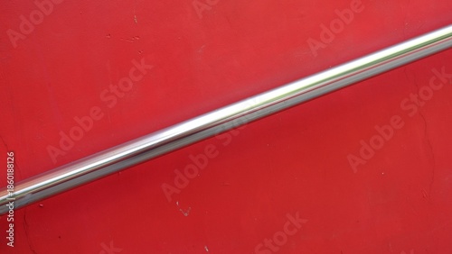 Fotografía Abstract minimalist close-up of a polished chrome handrail diagonally crossing a vibrant solid red wall