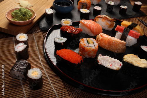 High-quality close-up of fresh assortment sushi rolls served on a dark plate, featuring vibrant colors, fresh fish, laid on slate board bamboo mat chopsticks
