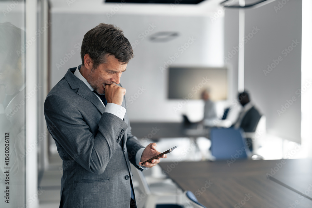 Fototapeta premium Coughing Businessman Checks Phone in Modern Office During Busy Workday