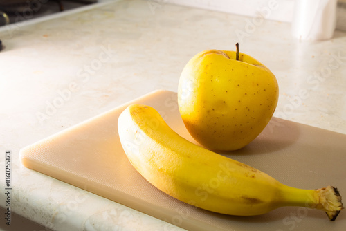 Fresh Yellow Apple and Ripe Banana on a Kitchen Cutting Board
