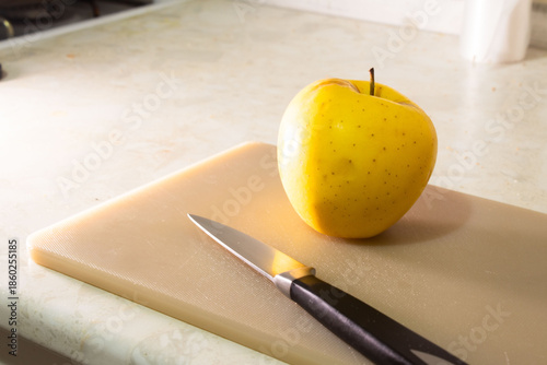 Single Yellow Apple and Kitchen Knife on a Plastic Cutting Board