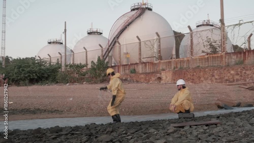 Workers collect samples near oil storage tanks at the shoreline in the evening light