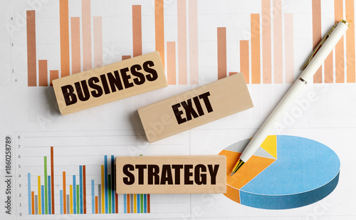 Wooden blocks with text business exit strategy on financial charts with white pen symbolizing planning and company transition