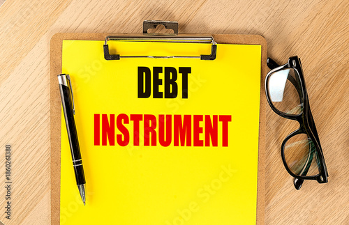 Clipboard with text debt instrument on yellow paper with pen and eyeglasses on wooden desk representing financial tools