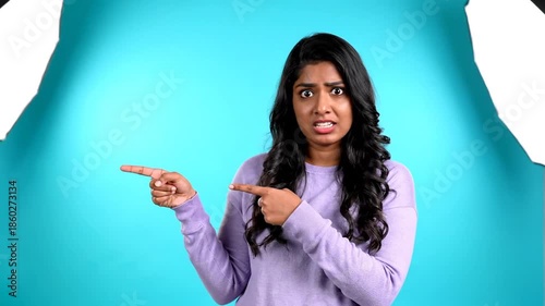 Surprised young woman pointing with both hands towards a blank space background for marketing,