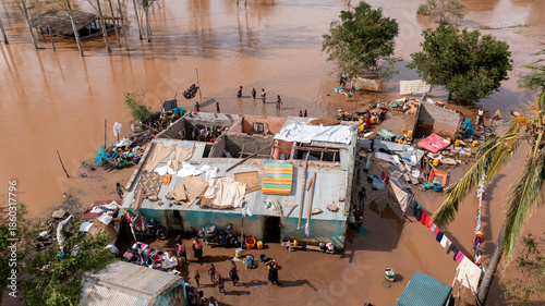 Aerial view of murky floodwaters engulfing homes, with only rooftops visible amid scattered debris and displaced people seeking refuge, Sofala Province, Mozambique.