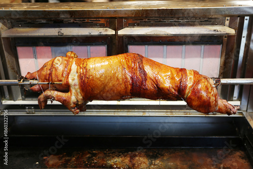 Grilled suckling piglet in spit roast. Traditional whole pig roasted on barbecue spit. Popular delicious and crispy roasted piggy on christmas fair