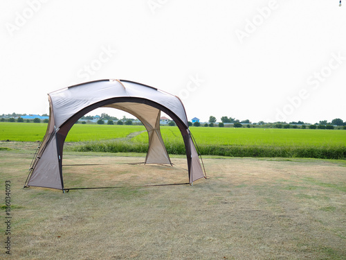 Portable canopy tent set on grassy field with green rice paddies, outdoor camping and rural landscape.