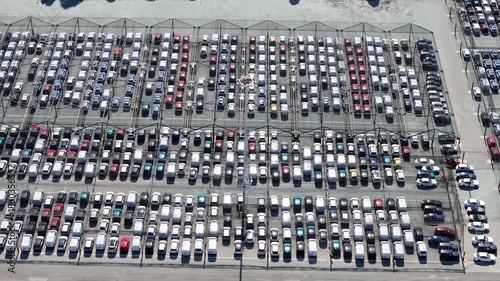 Aerial view of a vast parking lot filled with rows of cars, creating a geometric pattern of light and shadow,