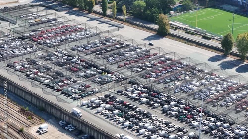 Aerial view of a vast parking lot filled with rows of cars, creating a geometric pattern of light and shadow,