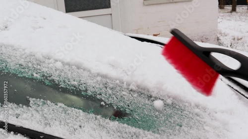 Male hand brushing fresh white snow off a car's windscreen after a blizzard. Winter vehicle maintenance and preparing for a safe drive