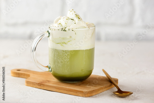 Green tea matcha latte with whipped coconut milk and pistachio with golden spoon on wooden board.
