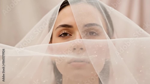 A woman with a veil covering her face looks directly at the camera in a video.