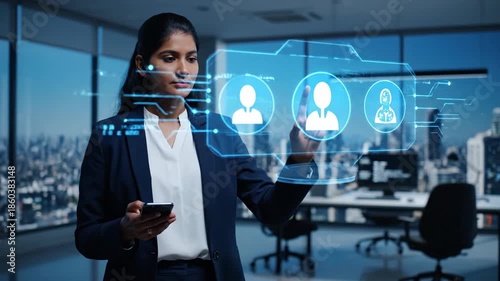 Wallpaper Mural Elegant Indian businesswoman using smartphone, interacting with a holographic CRM display of user profile icons in a modern high-rise office. Torontodigital.ca