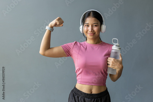 Foto Confident Asian woman wearing headphones and holding water bottle while flexing arm