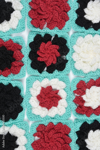 A collection of colorful crochet granny squares in black white and red with mint borders arranged for a blanket