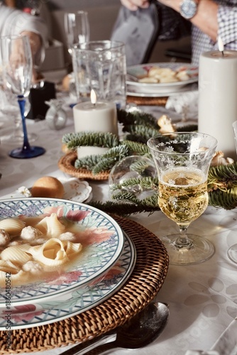 Christmas dinner table with traditional soup, candles, pine branches and elegant glassware. Mediterranean holiday celebration.