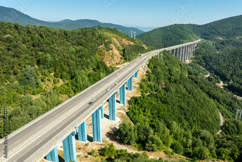 Aerial view of a highway viaduct bridge spanning a lush green mountain valley. Modern transportation infrastructure, engineering. Road trip travel