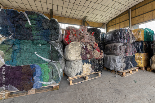 Warehouse with stacked bales of colorful recycled textile fibers. Sustainable raw material for the circular economy and fabric production in a factory.