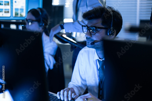 Vászonkép Focused male security operator with headset monitors data on screens in a high-tech control room
