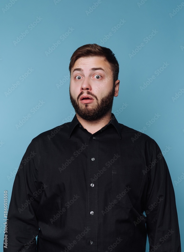 Fototapeta premium A surprised man with a beard and black shirt against a blue background.