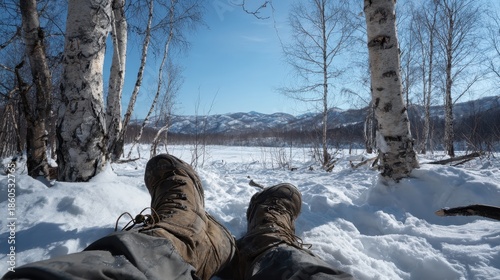 Booted legs resting in fresh snow with birch trees and distant hills, capturing a peaceful winter break in nature.

