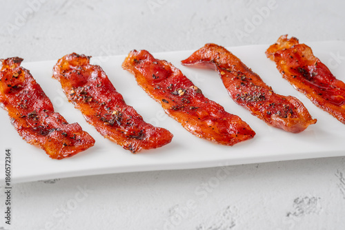 Billionaire bacon strips glazed with pepper and chili flakes on minimalist plate