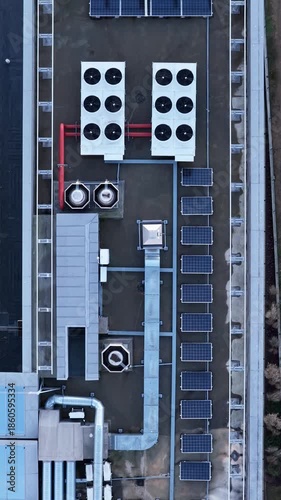 Symmetrical aerial view of a commercial building rooftop showing solar panels, HVAC fans, ventilation ducts, and cooling systems, illustrating modern sustainable building infrastructure.