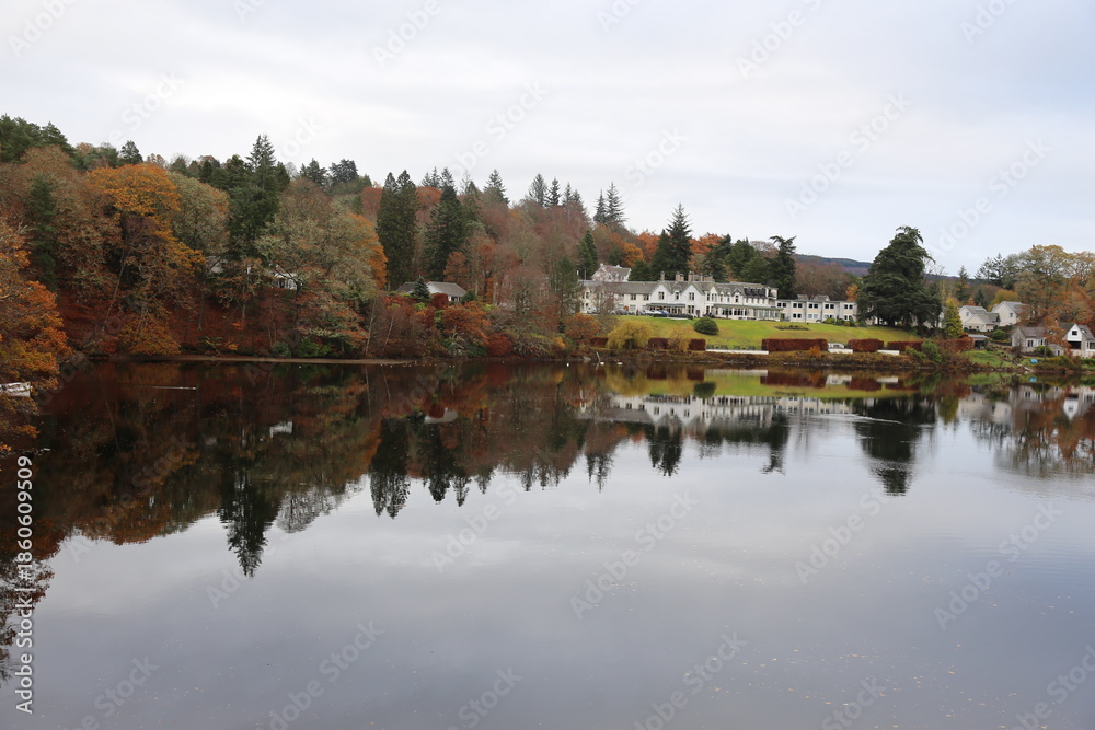 Fototapeta premium Peaceful Autumn Loch with Forest Reflections and Highland Village in Pitlochry, Scotland.
