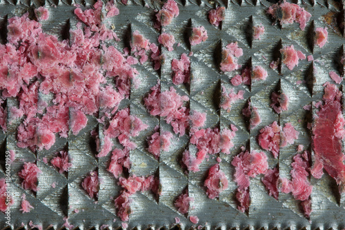Jagged metal teeth of the rasp trap red plastic fragments. An abstract rhythm of shape, color, and texture, frozen in a single moment.