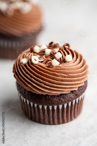 Chocolate cupcake topped with smooth swirled chocolate cream cheese frosting and white chocolate curls on a light stone background.