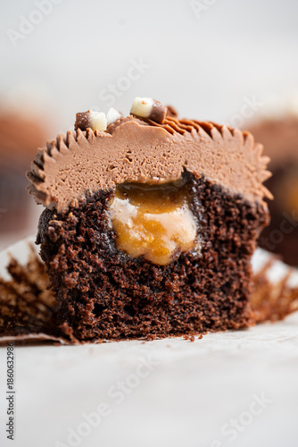 Cut chocolate cupcake revealing gooey caramel nut filling topped with chocolate cream cheese frosting, styled as a rich indulgent dessert close up.