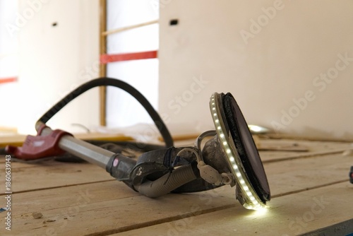 Sanding a ceiling during a home renovation.A construction worker sands a ceiling with an electric drywall sander. Electric drywall sander with LED light.