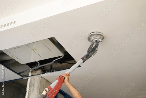 Sanding a ceiling during a home renovation.A construction worker sands a ceiling with an electric drywall sander. Electric drywall sander with LED light.