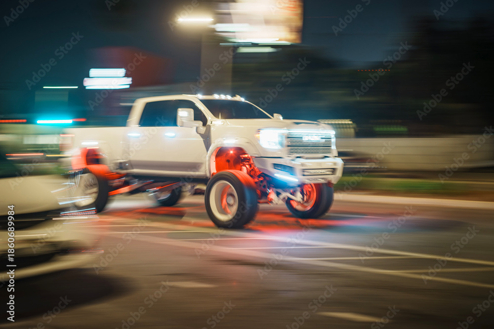 Fototapeta premium LOS ANGELES, CA - October 09, 2025: Custom GMC Sierra lifted lifestyle pickup truck with TIS Wheels driving on dark city street at night. Urban road background is blurred in motion.