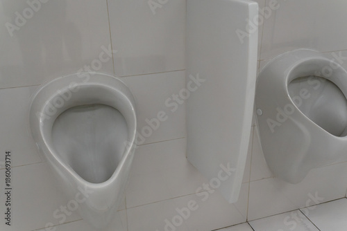 White ceramic urinal on tiled wall in public restroom. Minimalist restroom design with sleek urinal and sterile tiled surfaces in urban infrastructure