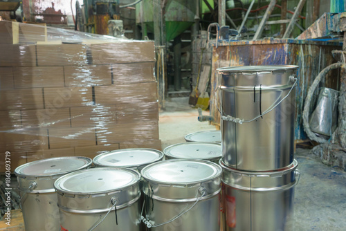 Chemical storage in a manufacturing plant with signs of recent use and logistical preparation. Sealed paint containers and stacked boxes in a production facility interior
