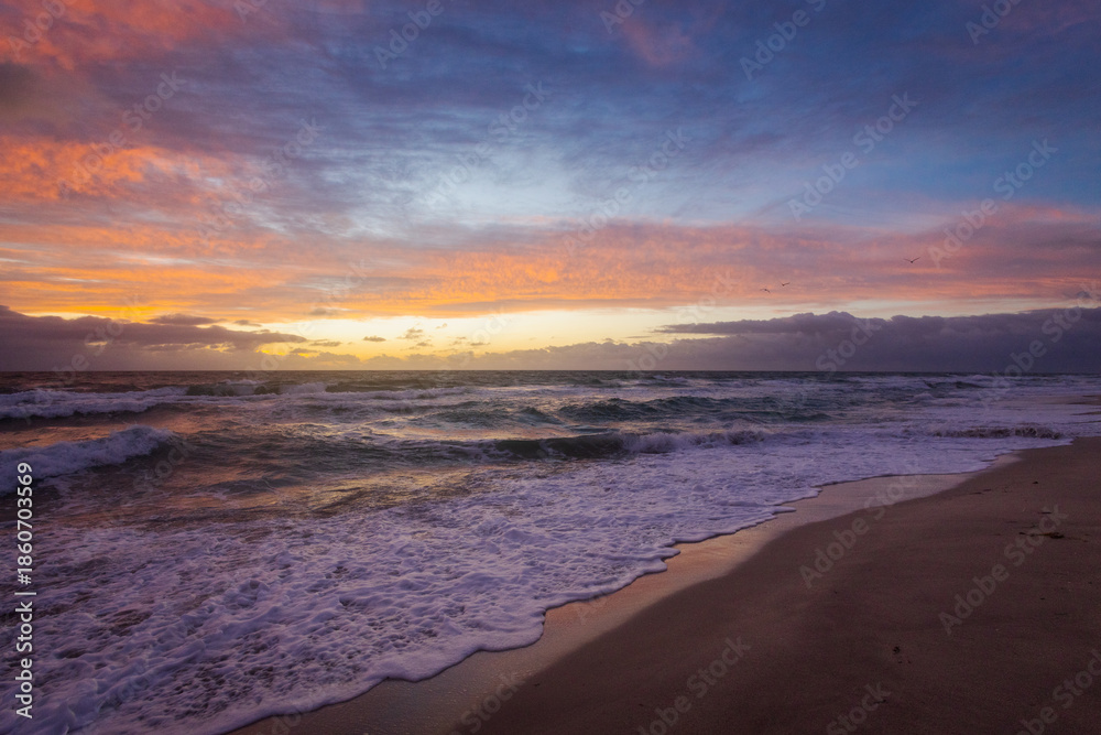 Obraz premium Colorful Sunrise Over Ocean Waves and Sandy Beach